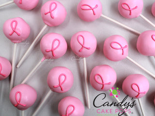 Breast Cancer Awareness Pink cake pops decorated with a pink ribbon symbol, arranged on a light background. The brand name 'Candy's Cake Pops' is visible as a watermark and logo. 