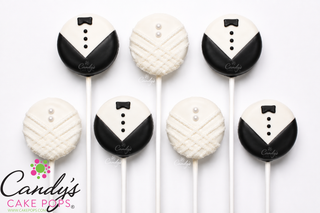 Six round cake pops decorated to look like tuxedo grooms, arranged on a white background. Three are dressed as black and white tuxedo jackets with small black bow ties and white buttons, and three are dressed as white brides dress with small white pearl details.