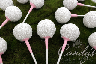 Golf Ball Cake Pops with light pink tees arranged on a green moss-like surface. A Candy's Cake Pops watermark is visible.